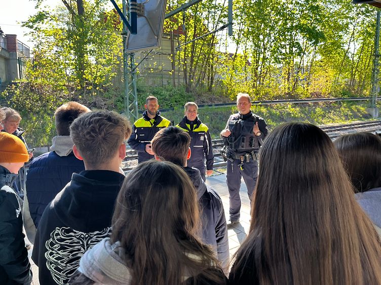 Kolleg:innen des DB Sicherheits Präventionsteams zusammen mit der Bundespolizei im Gespräch mit einer Gruppe Schülern am Bahnhof