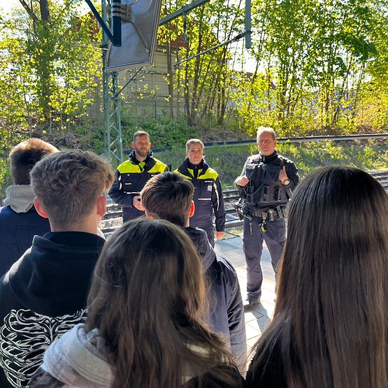Kolleg:innen des DB Sicherheits Präventionsteams zusammen mit der Bundespolizei im Gespräch mit einer Gruppe Schülern am Bahnhof