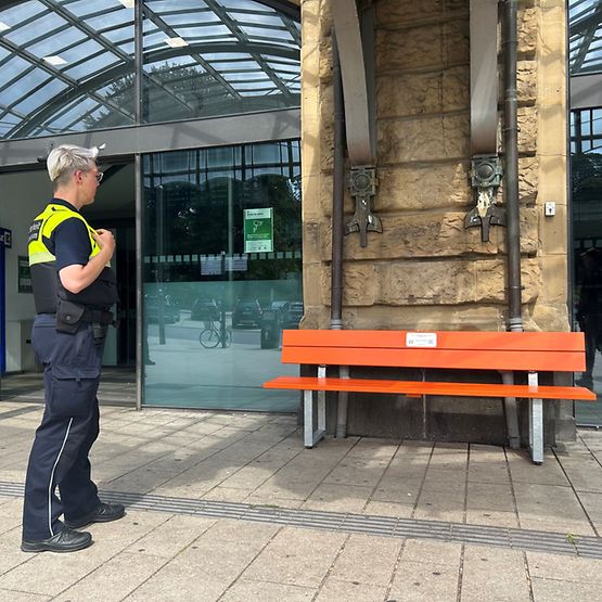 Kollegin der DB Sicherheit steht vor der orangenen Bank am Bahnhof Hamburg Dammtor