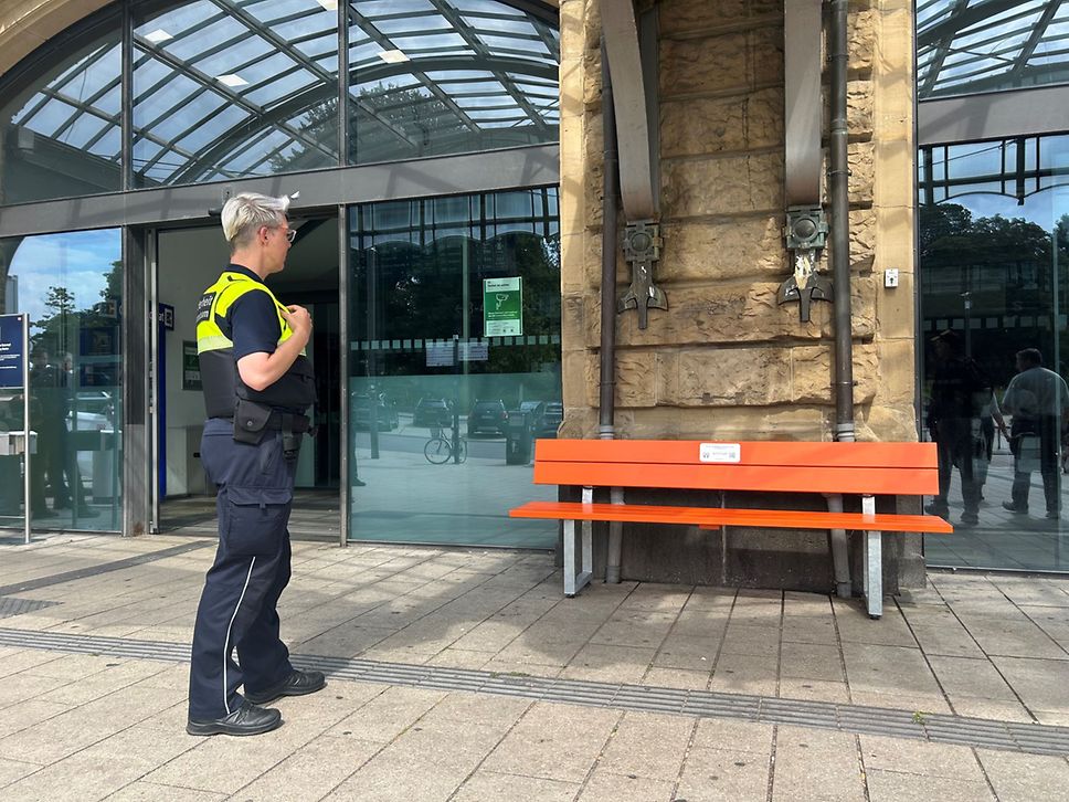 Kollegin der DB Sicherheit steht vor der orangenen Bank am Bahnhof Hamburg Dammtor